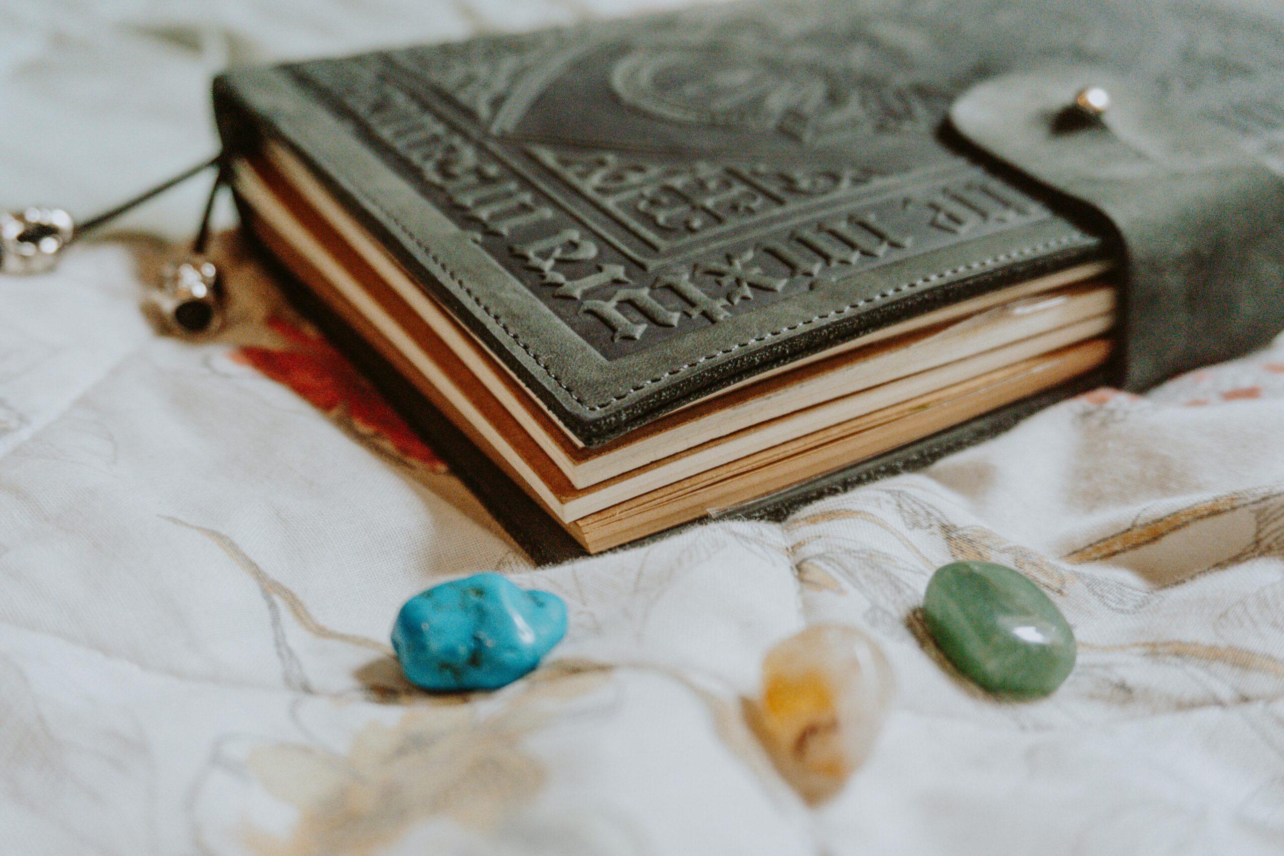 An antique-style leather journal with gemstones rests on floral bedding, suggesting creativity.