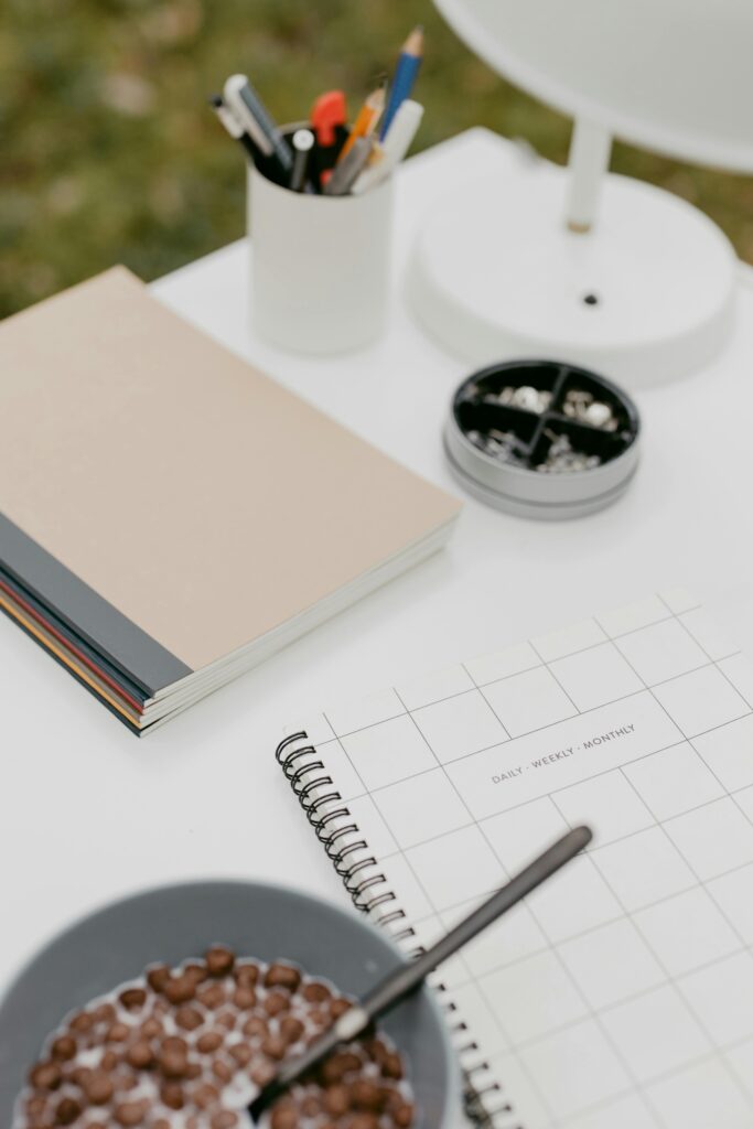 A modern workspace with notebooks, cereal, and office supplies on a white desk.