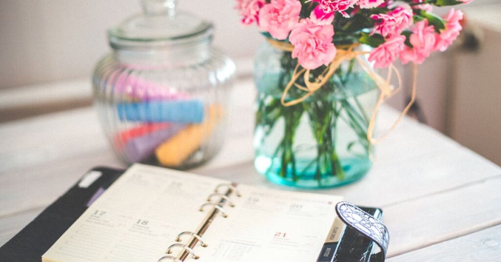 A chic desk setup with an open planner and a vase of pink flowers, ideal for productivity.