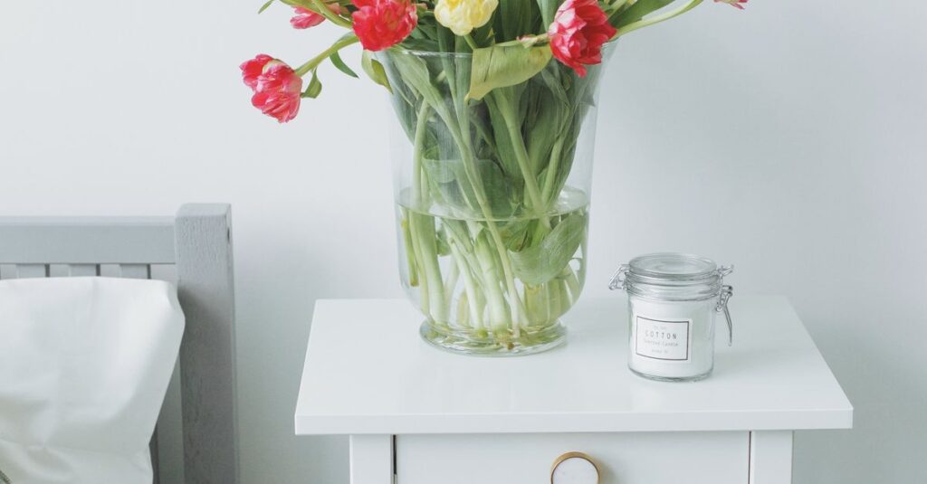 Minimalist bedroom decor featuring a vase of tulips on a white nightstand, creating a cozy ambiance.