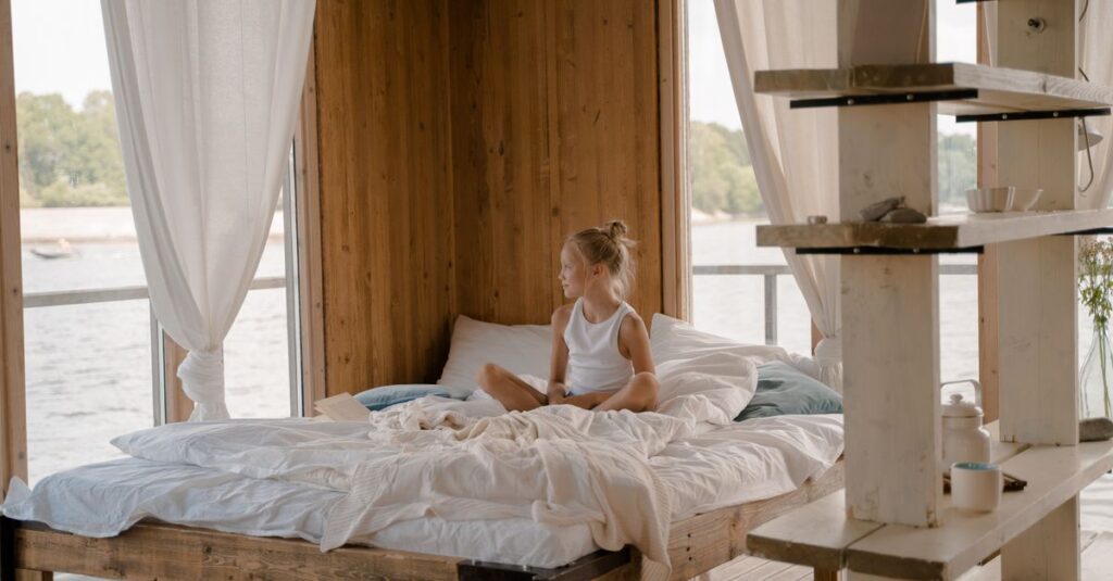 A child enjoys a serene moment in a cozy bedroom with a view of the lake.