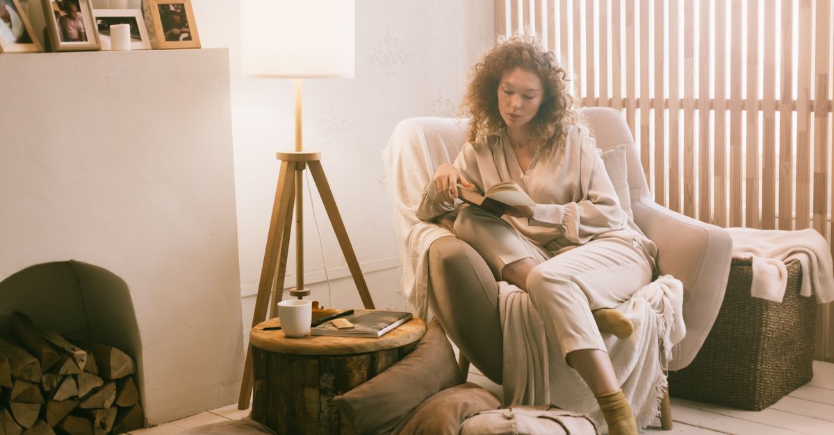 Woman relaxing in a cozy armchair at home, enjoying a book in a warmly lit room.