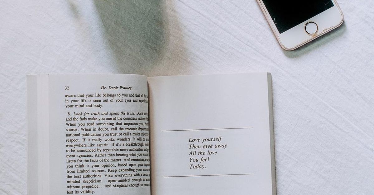 Minimalist arrangement featuring a coffee cup, open book, and smartphone on a white surface.