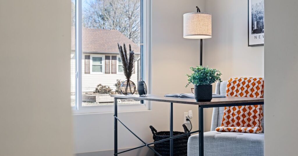 Bright modern home office with a minimalist desk, lamp, and cozy blanket by the window.