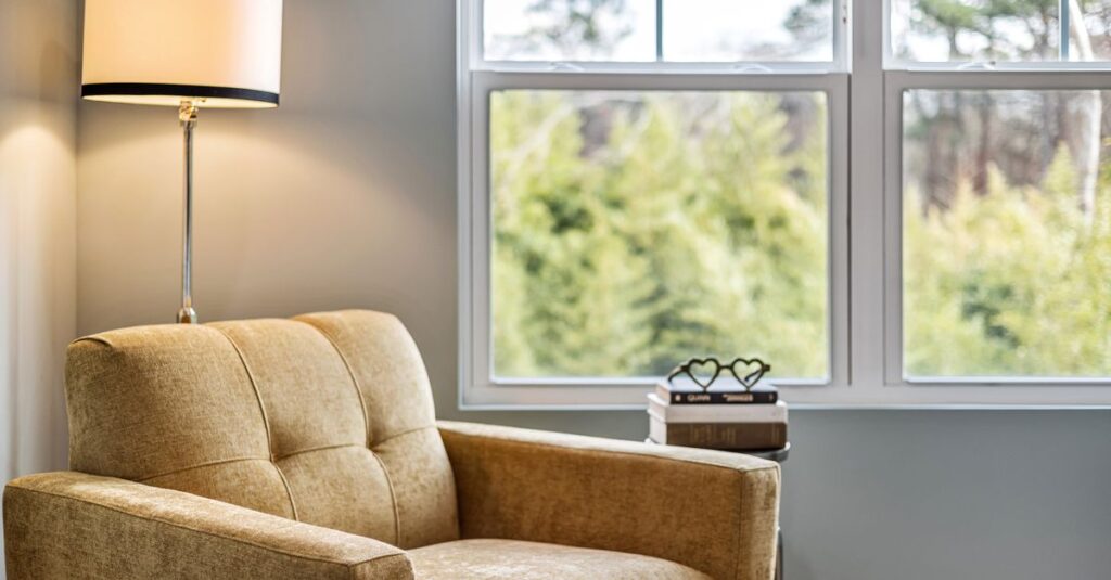 Modern living room with cozy armchair, footstool, and large window view.