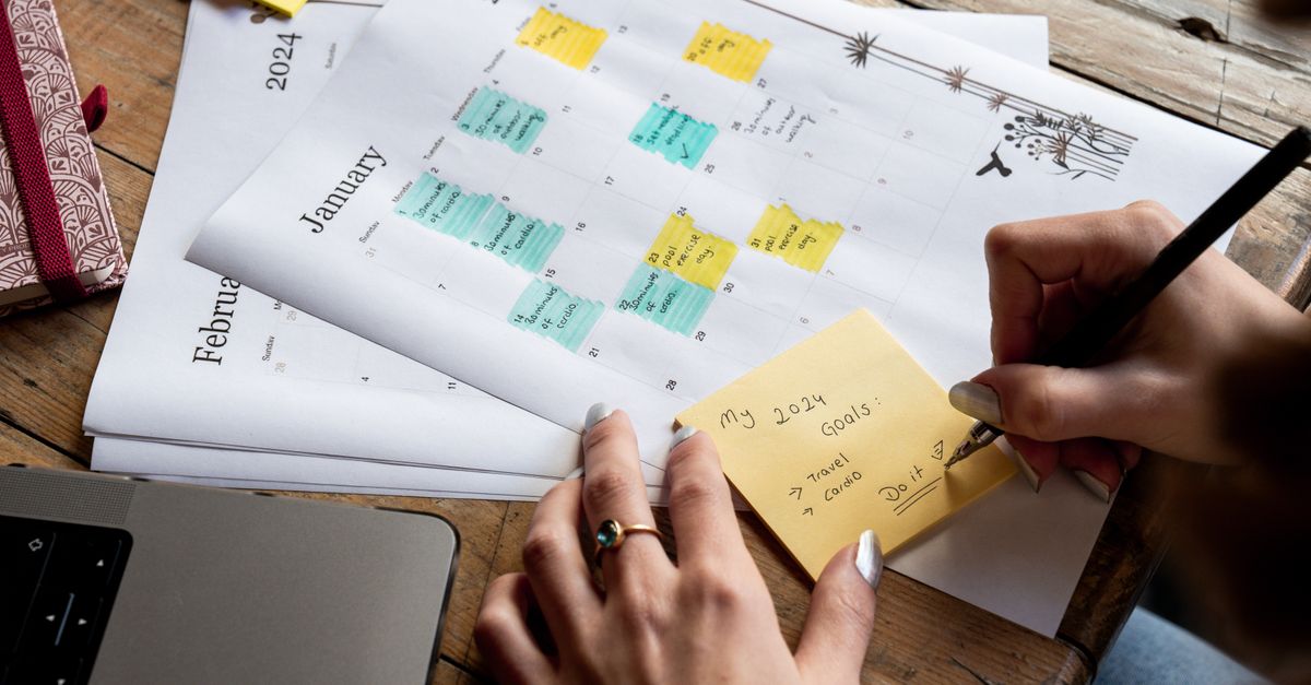 Close-up of a person writing new year's goals on a sticky note with a 2024 calendar in the background.