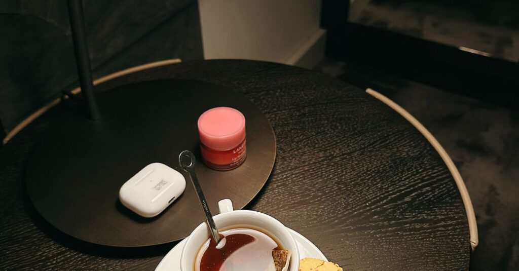 A warm cup of tea with a macaron on a side table under soft indoor lighting.