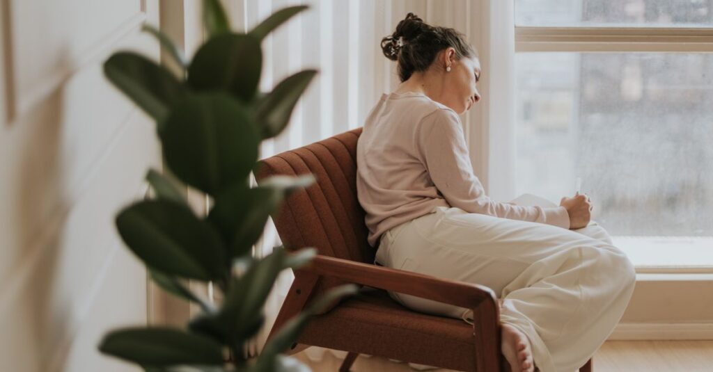 Woman relaxing on a chair by a window, deep in thought, indoors.