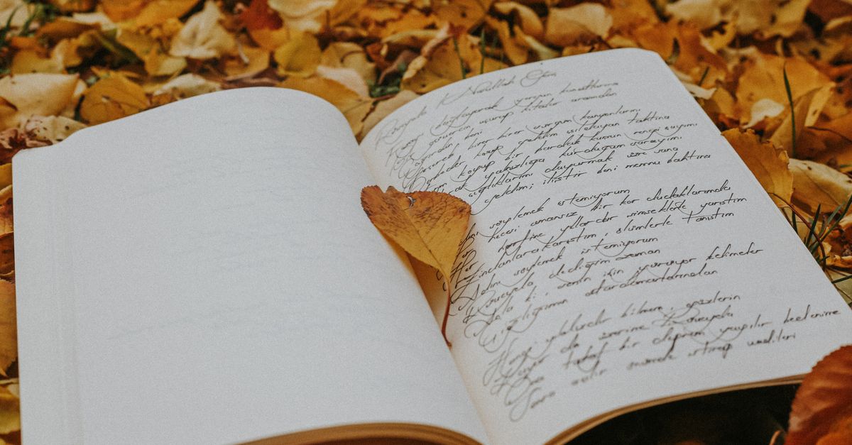 Open journal with cursive writing amidst vibrant autumn leaves.
