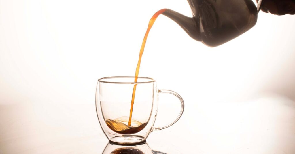 Elegant tea being poured from teapot into glass cup, with reflection.