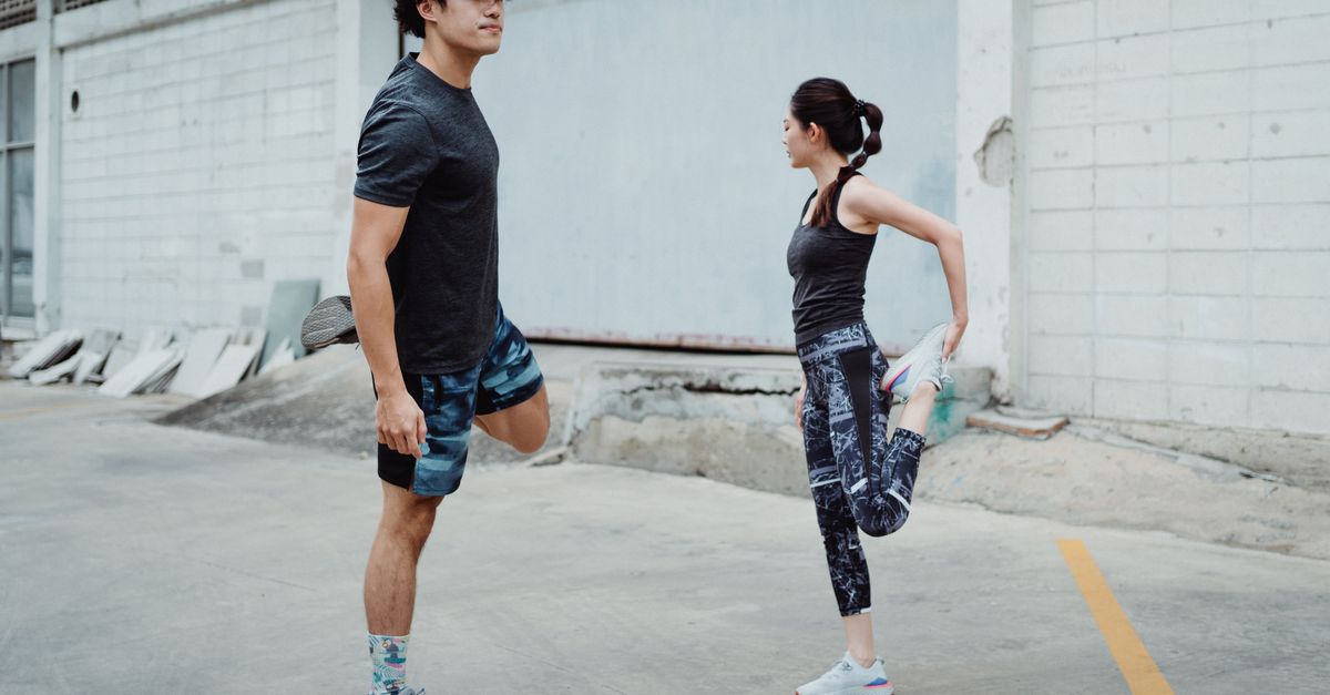 Two people stretching outdoors, focusing on balance and fitness in an urban setting.