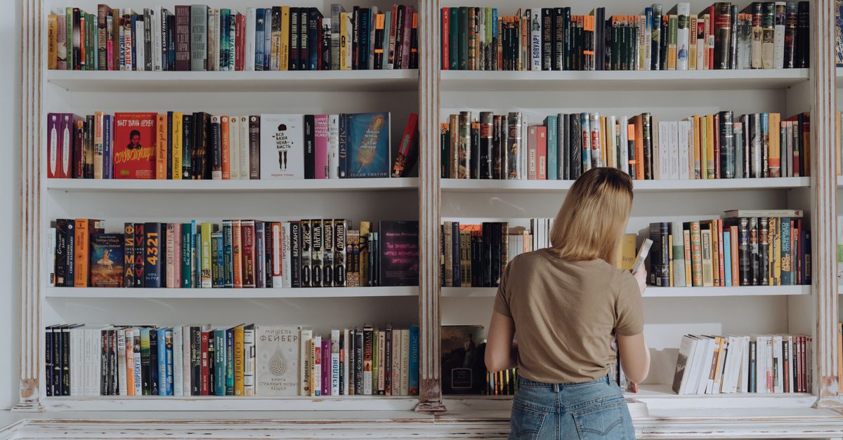 Blonde woman browsing a bookshelf in a library, conveying a love for reading and literature.