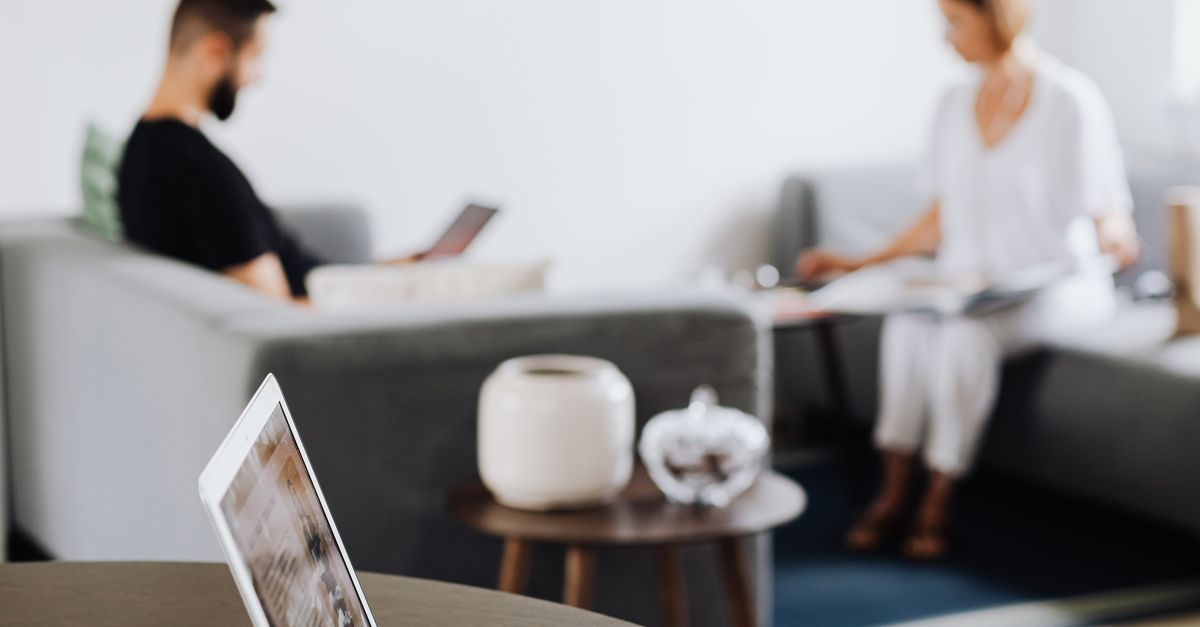 A cozy living room with a focus on a laptop, while two adults relax in the background, showcasing a modern lifestyle.