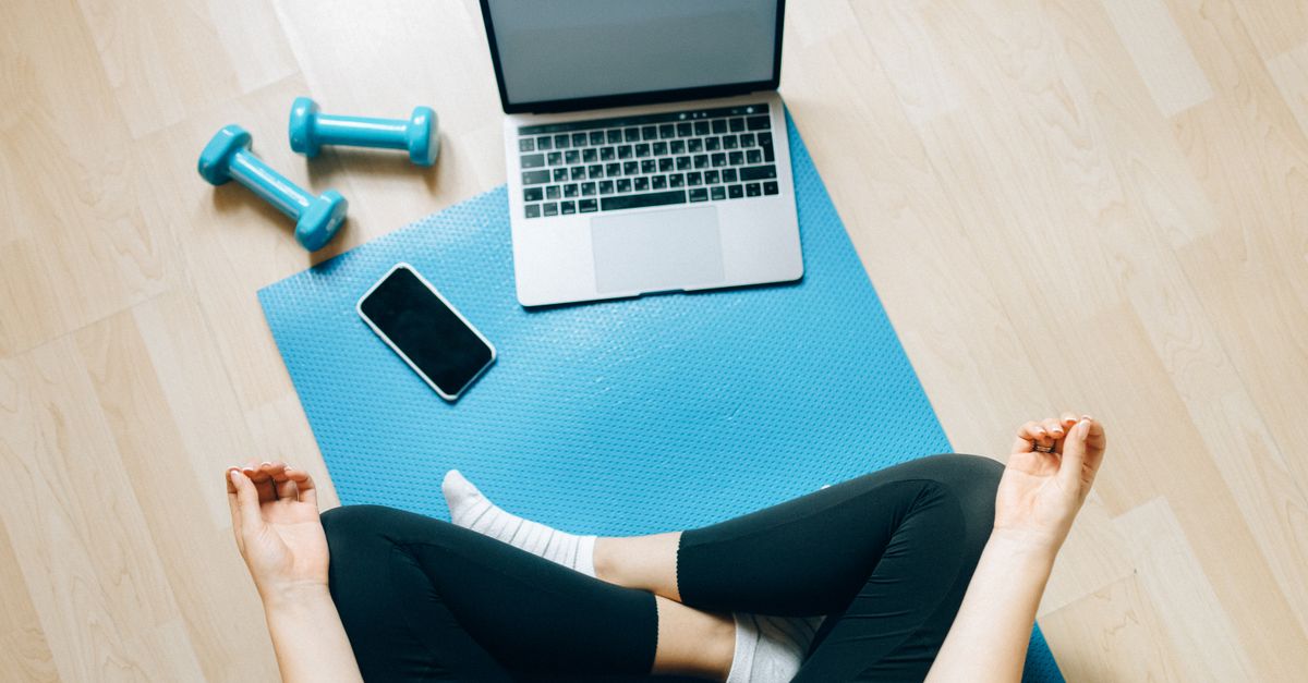 Yoga mat setup with laptop and dumbbells for home fitness.