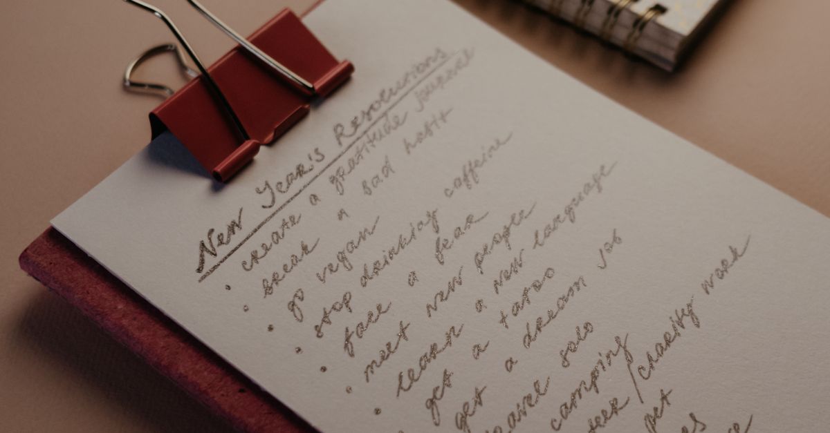 A flat lay of a clipboard with New Year’s resolutions and a notebook on a desk.