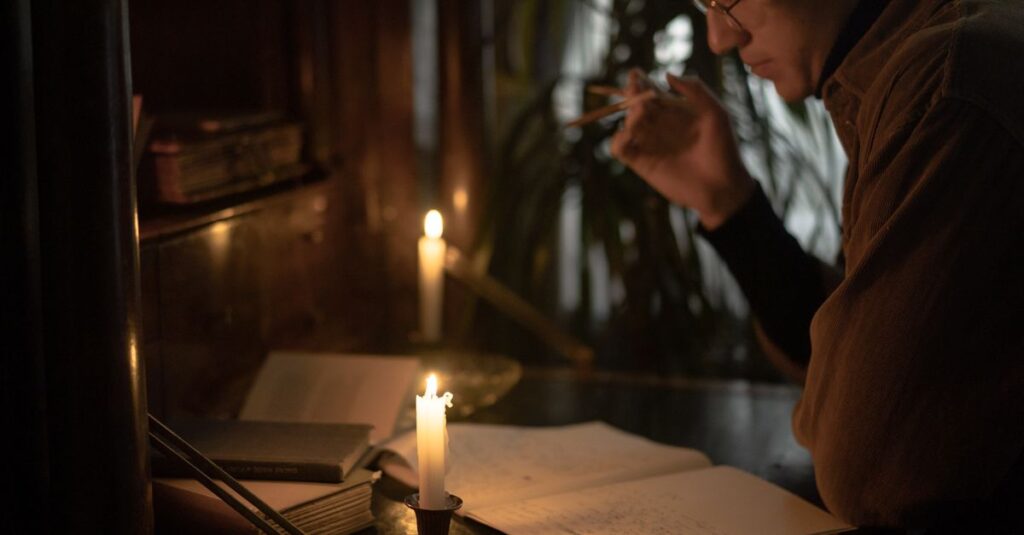 A person reads and writes by candlelight, creating a moody and contemplative atmosphere.