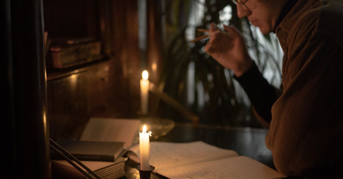 A person reads and writes by candlelight, creating a moody and contemplative atmosphere.