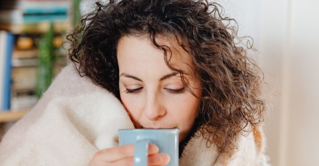 Woman wrapped in a warm scarf enjoying a hot drink, capturing a peaceful cozy indoor moment.