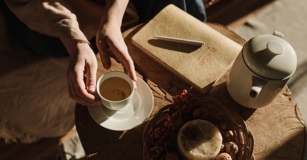 Cozy indoor setting with hands holding tea, notebook, and teapot, basking in warm autumn sunlight.