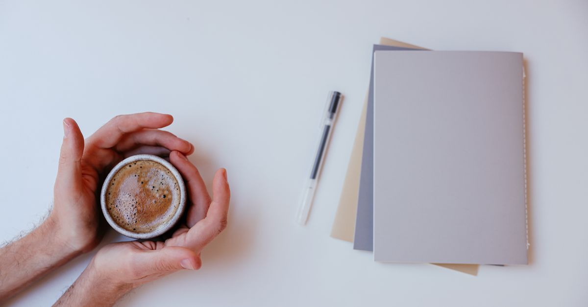 A warm coffee surrounded by notebooks and pen on a white background, perfect for productivity.