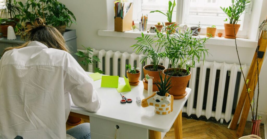 A woman in a cozy indoor workspace with potted plants and natural light.
