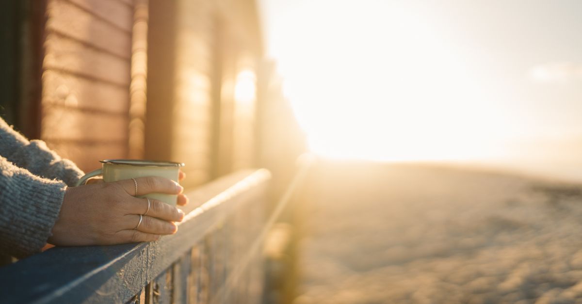 A serene morning scene with a hand holding a mug at sunrise, capturing warmth and tranquility.