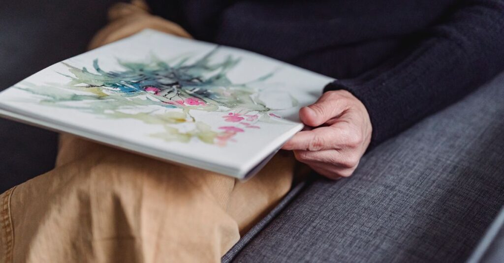 A person holds a watercolor sketchbook with vibrant botanical artwork.