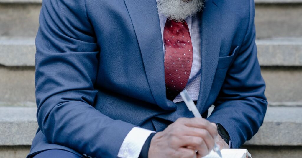 African American man writing in notebook on stairs wearing a suit, focusing on work.
