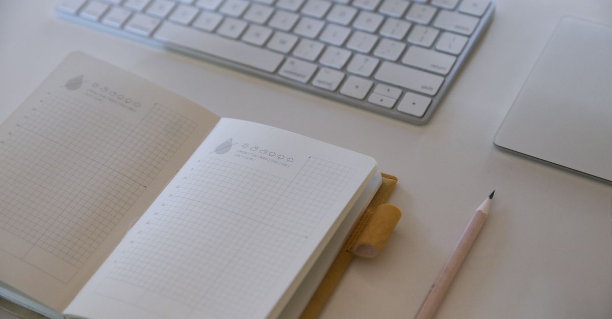 A clean and simple workspace featuring a keyboard, notebook, and pencil.