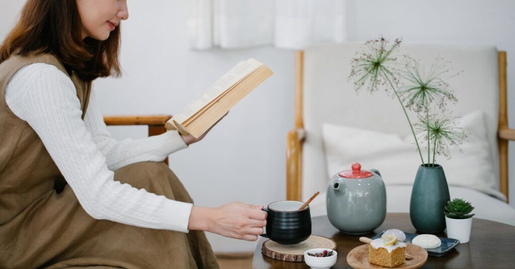 A young woman enjoys reading a book while drinking tea in a cozy indoor setting.