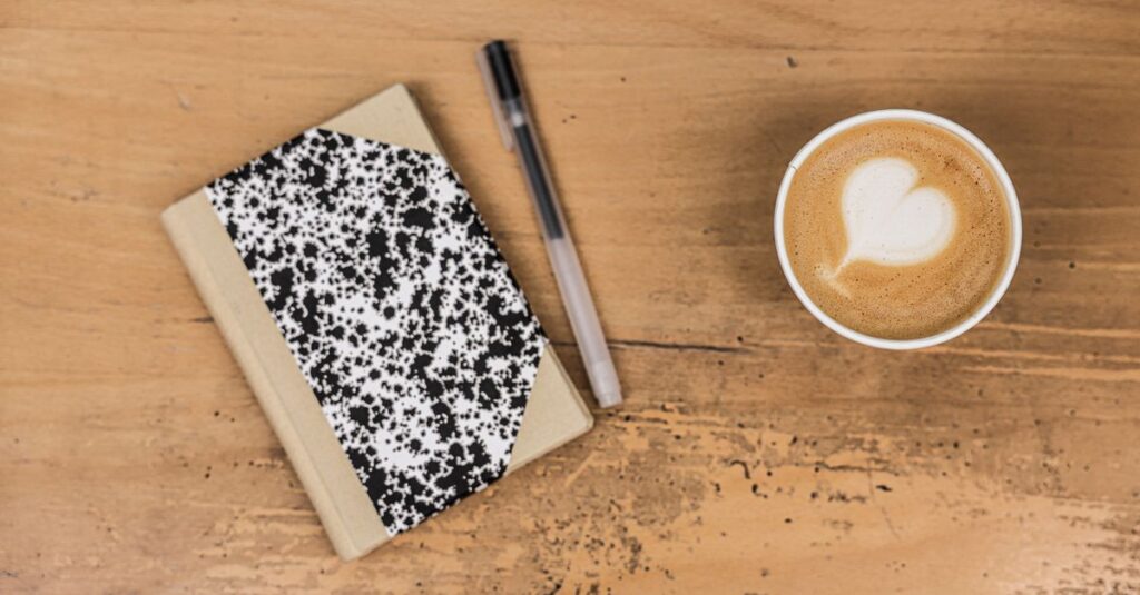 A comforting flatlay featuring a latte, marble notebook, and pen on a wooden table.