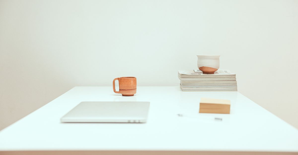 Simple minimalist workspace featuring a laptop, mug, and stacked magazines.