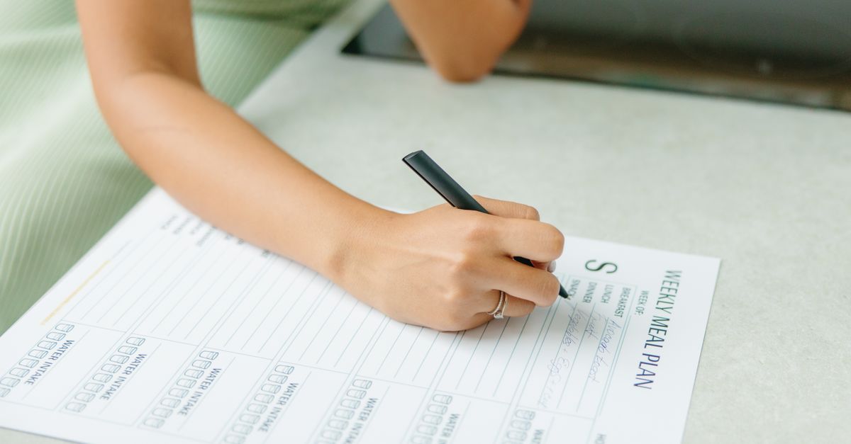 Close-up of a woman writing a weekly meal plan at home, promoting a healthy lifestyle.