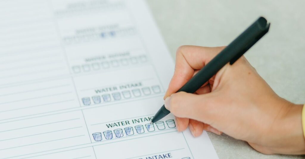 Hands filling out a nutrition plan with a focus on water intake. Ideal for health and wellness themes.