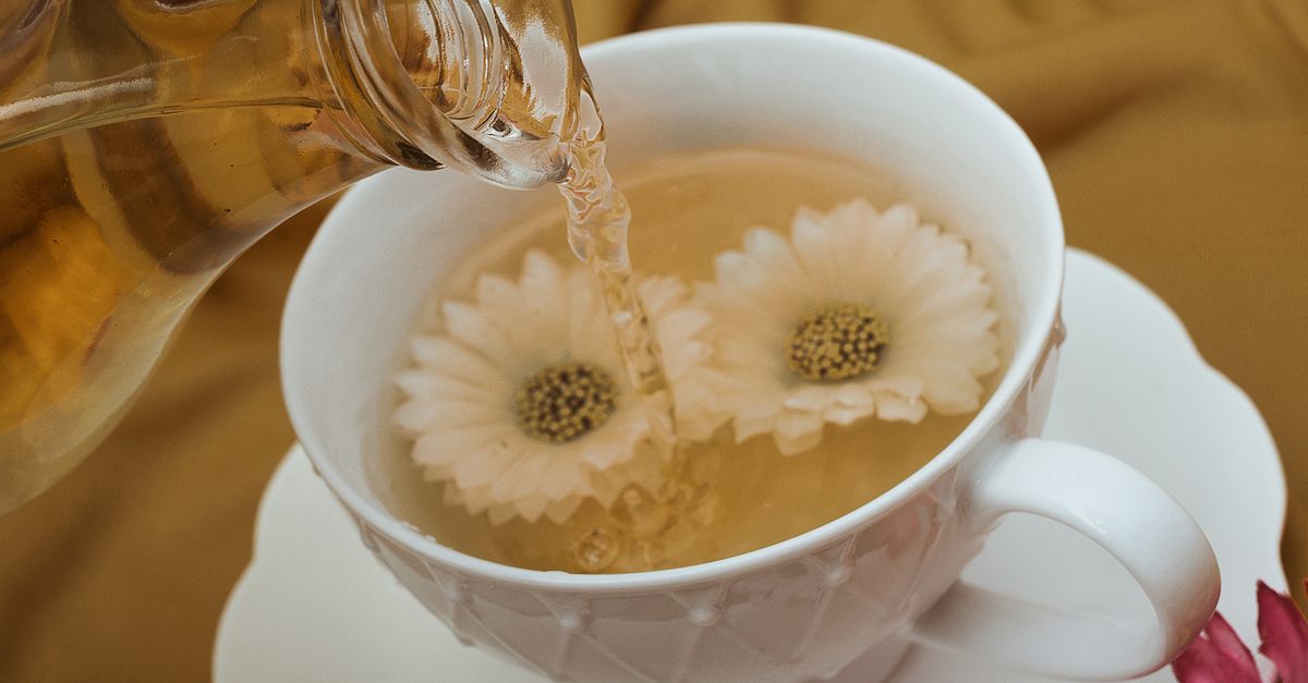 Close-up of herbal tea being poured into a white teacup with floating flowers, creating a serene and relaxing scene.