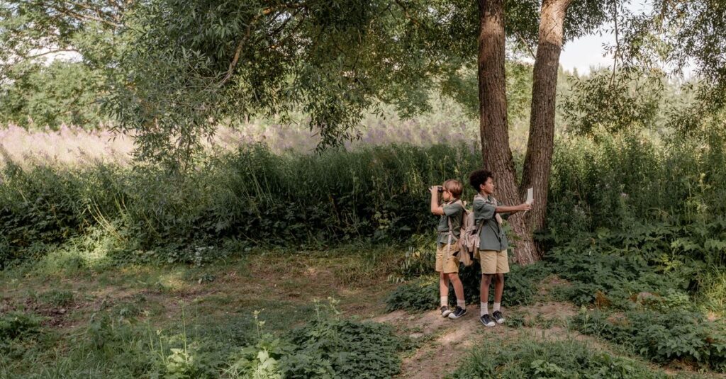 Two children exploring nature by a tree in a lush green outdoor setting, capturing moments.